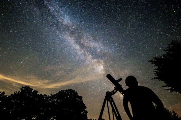Man with telescope in front of night sky